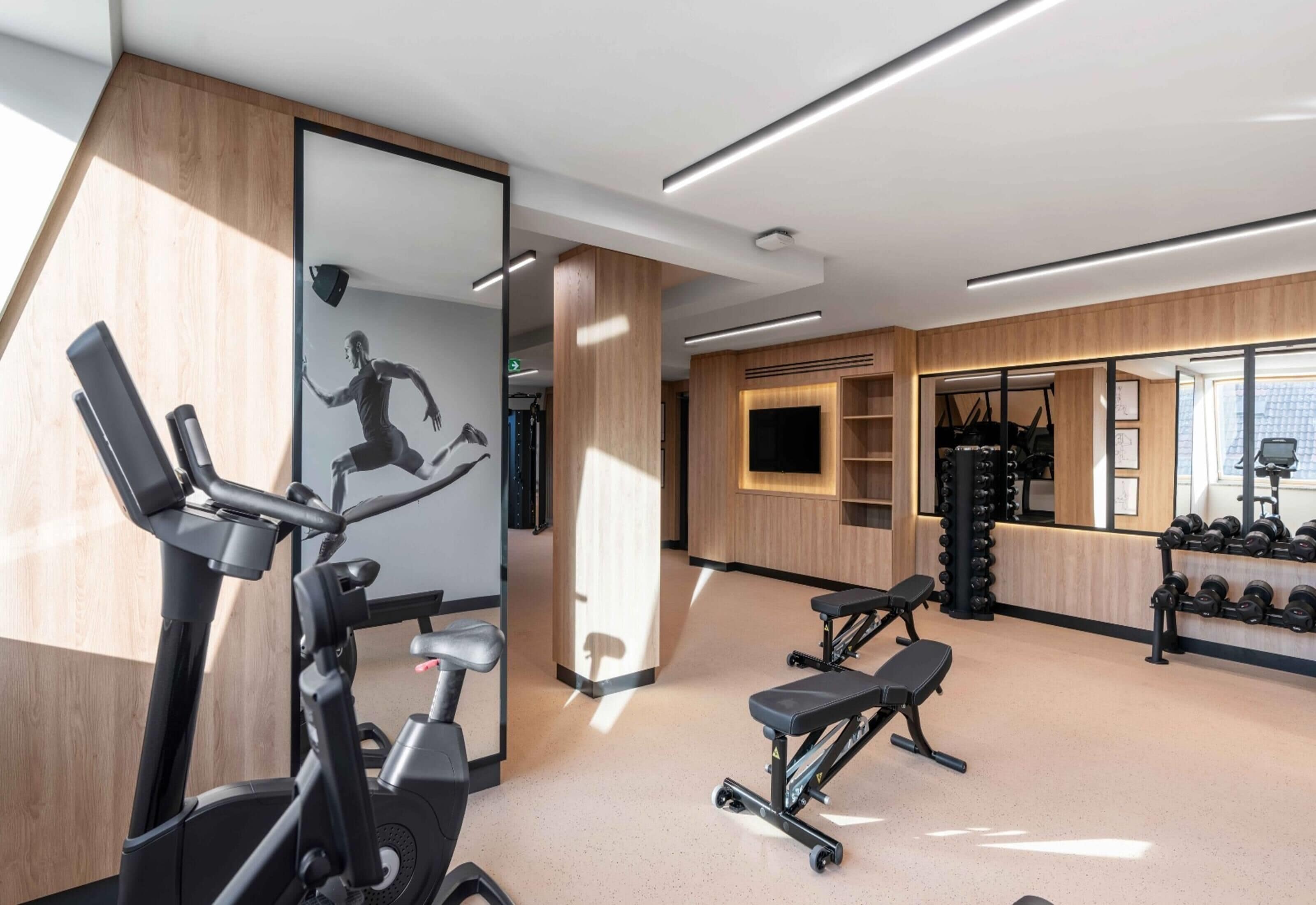 A modern gym with exercise equipment, a large mirror, and a wall-mounted TV.