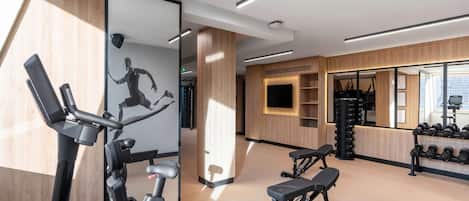 A modern gym with exercise equipment, a large mirror, and a wall-mounted TV.