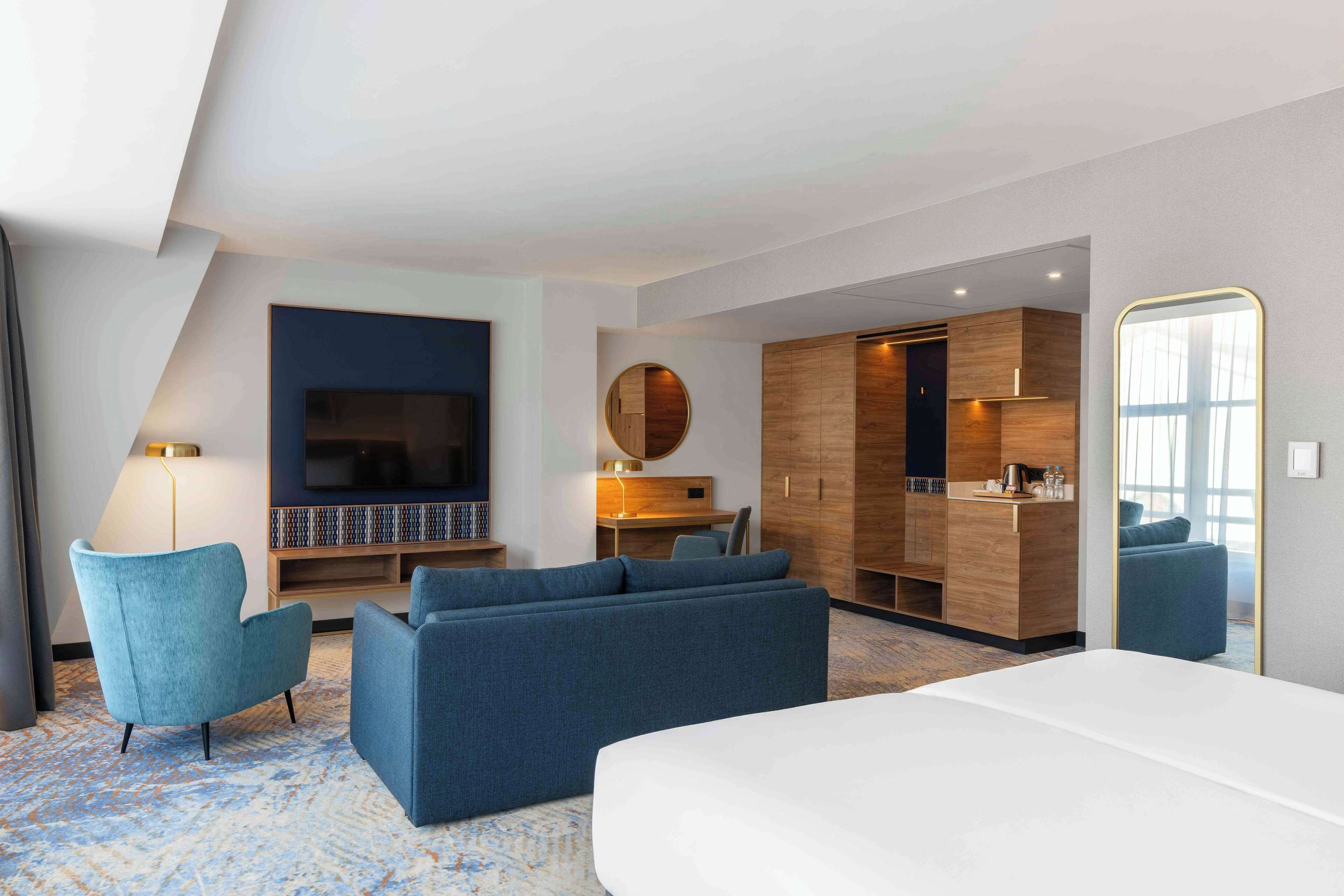 Una habitación de hotel moderna con una cama grande, un sofá, un televisor, un escritorio y un armario.
