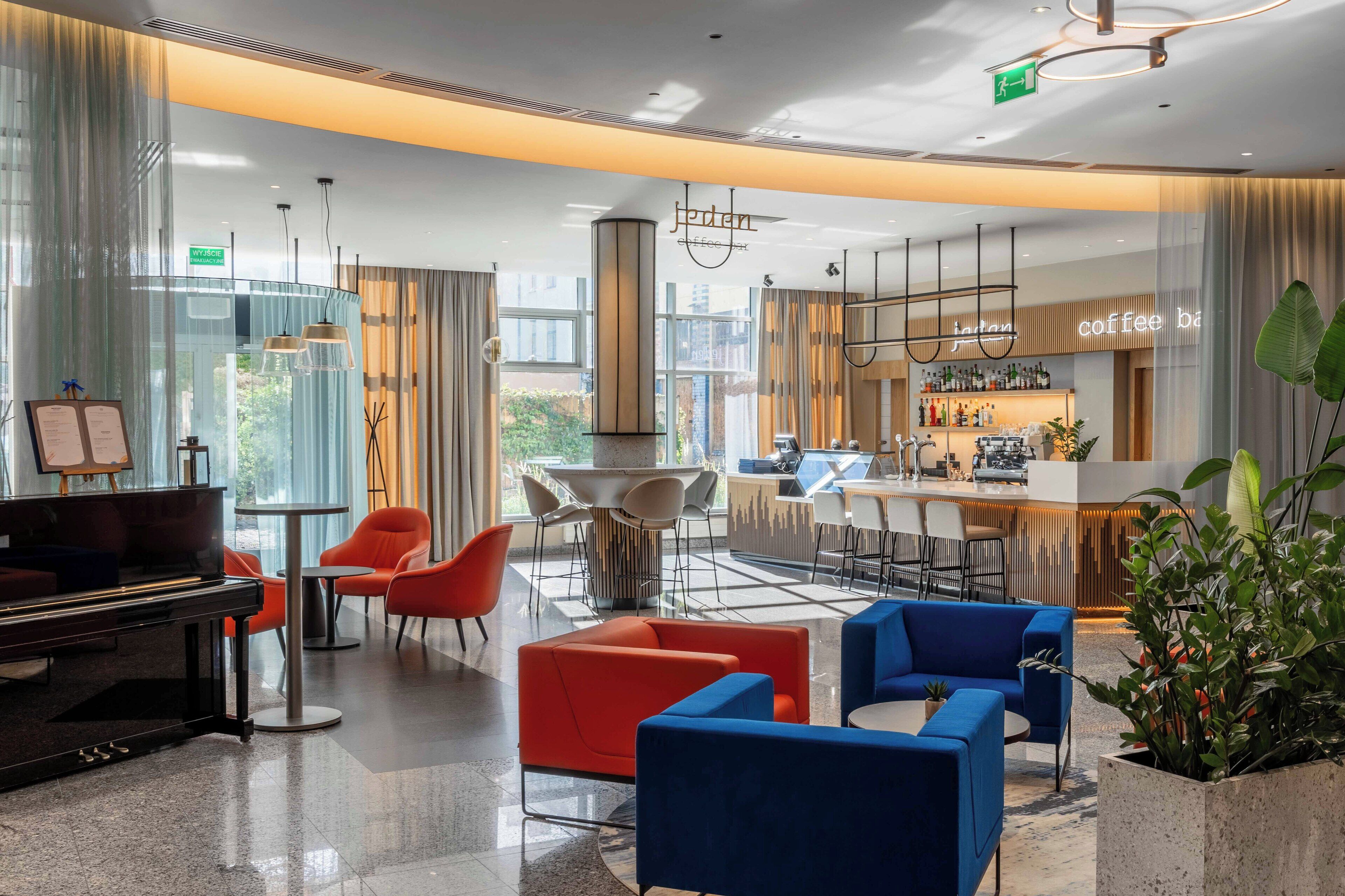 A modern lobby with a piano, seating areas, a bar, and large windows.