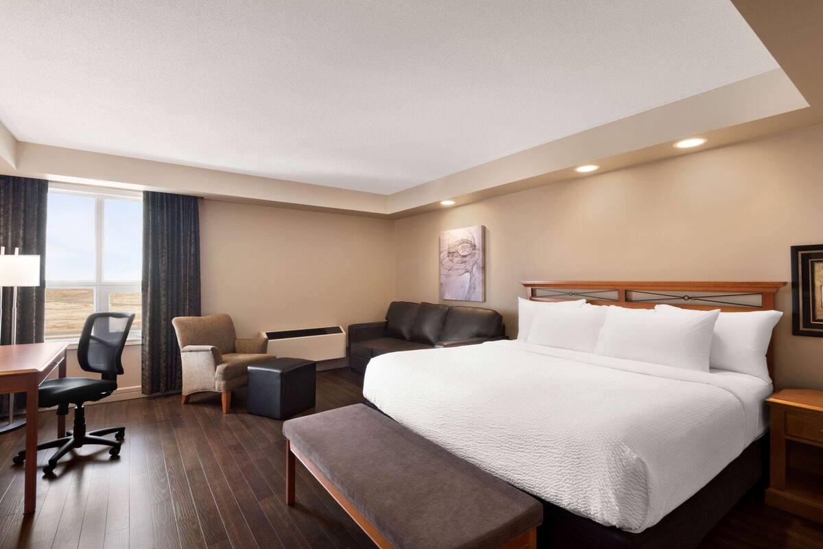 Habitació d'hotel amb un llit gran, un escriptori, una cadira, una banca i vista a l'exterior.