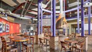 Un restaurante espacioso con techos altos, conductos expuestos y diferentes opciones de asientos, incluyendo mesas y sillas.