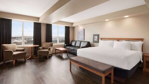 Habitación de hotel con una cama grande, dos sillones, una mesita, un sofá y vistas a la ciudad a través de amplias ventanas.