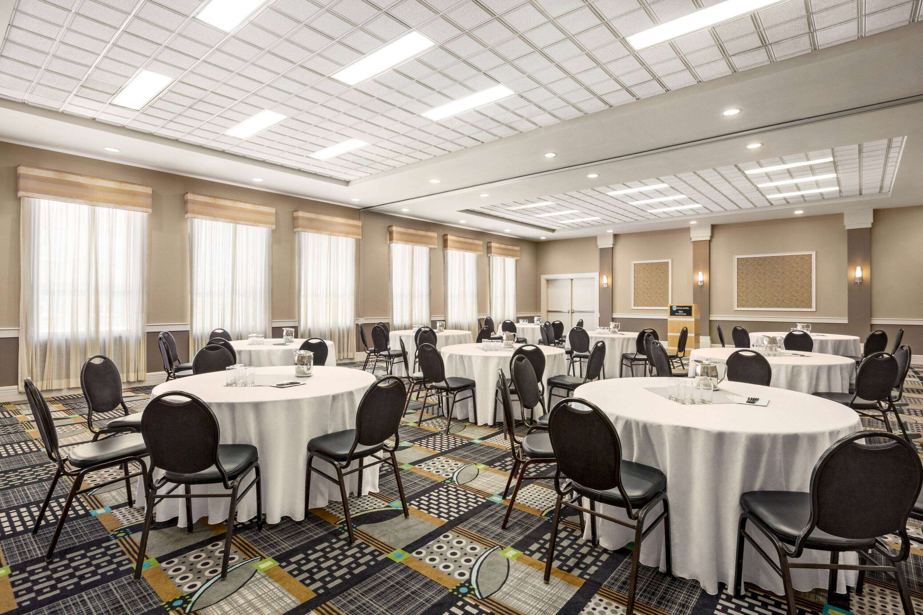 A conference room with multiple round tables, black chairs, and a patterned carpet.