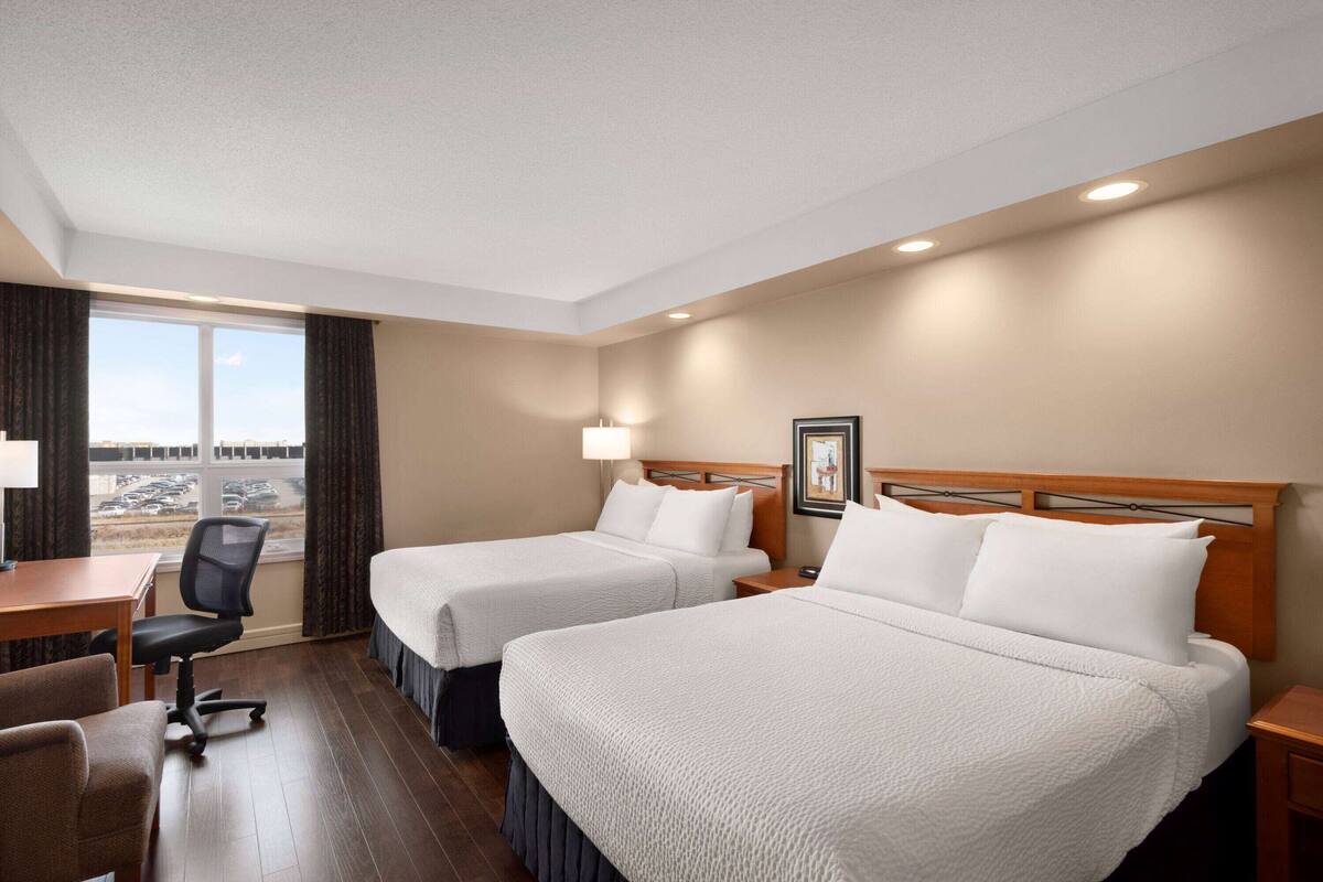 Habitació d'hotel amb dos llits, una taula de treball, una cadira i una finestra que dona a un pàrquing.