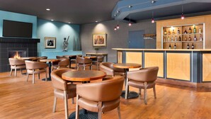 Un área de bar moderna con mesas y sillas de madera, una exhibición de botellas de licor y una chimenea.
