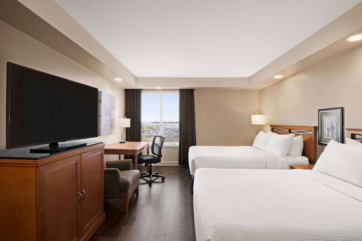 Habitació d'hotel amb televisió de pantalla plana, escriptori amb cadira, dos llits i finestra amb vista a un pàrquing.