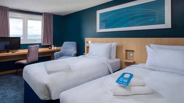Habitación de hotel con dos camas, un escritorio, un televisor y una ventana con cortinas.