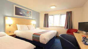 Ein Hotelzimmer mit zwei Betten, einem Schreibtisch mit Computer, einem Fernseher und einem Fenster mit Vorhängen.