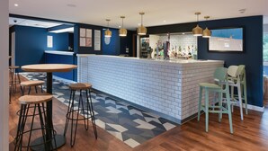 A modern bar area with a white brick counter, wooden stools, and pendant lighting. - Travelodge Ashford (Ashford)
