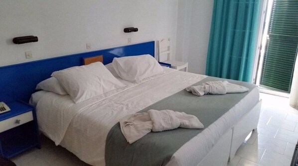 A neatly made bed with white linens and a grey blanket, a blue headboard, and a white bedside table with a phone. - Belle Helene Hotel (Corfu)