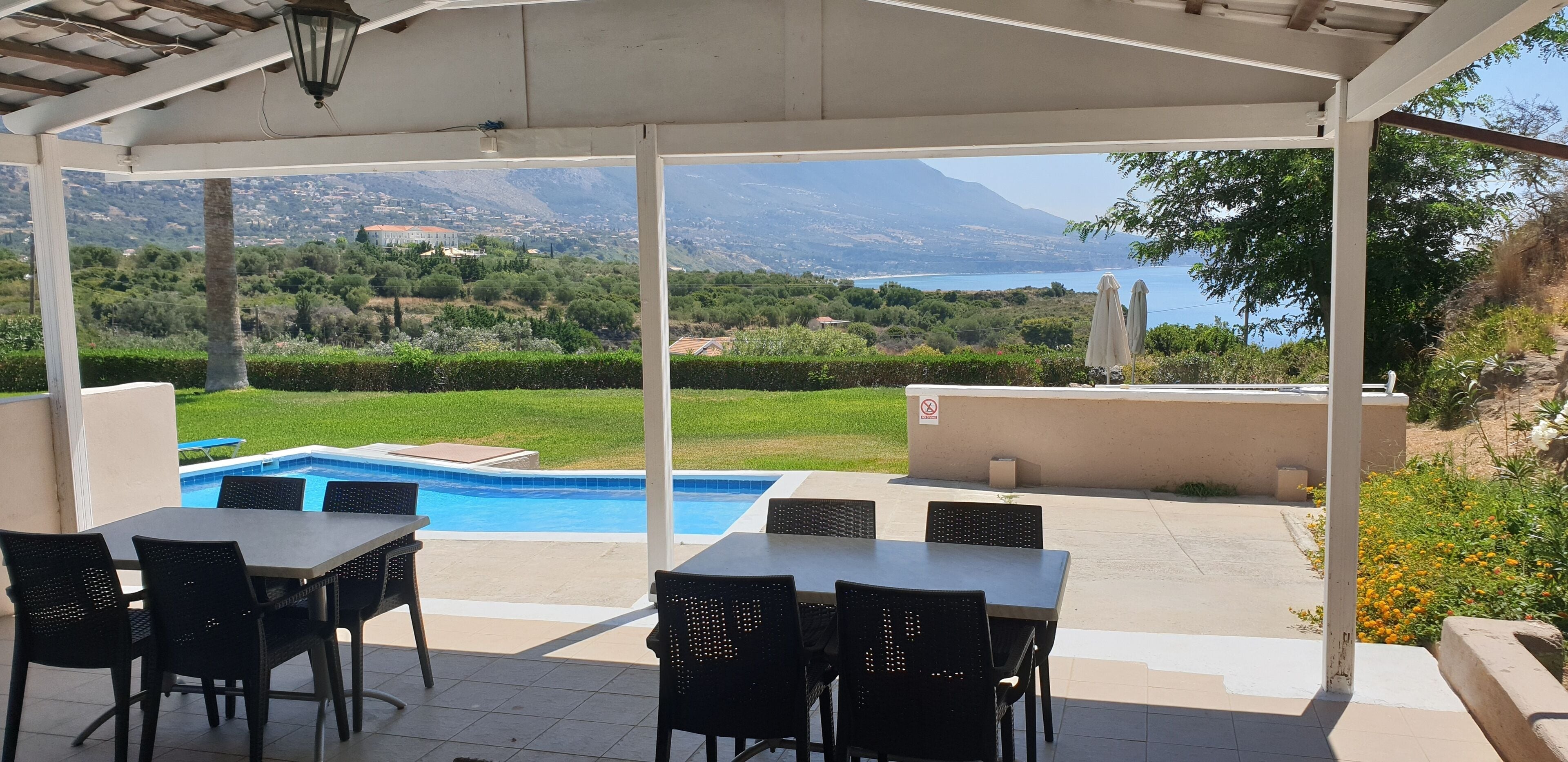 Un espacio al aire libre cubierto con piscina, mesas y sillas, con vistas a un paisaje pintoresco con montañas y una masa de agua.