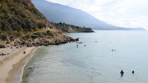 Una playa con agua cristalina, acantilados rocosos y montañas al fondo.