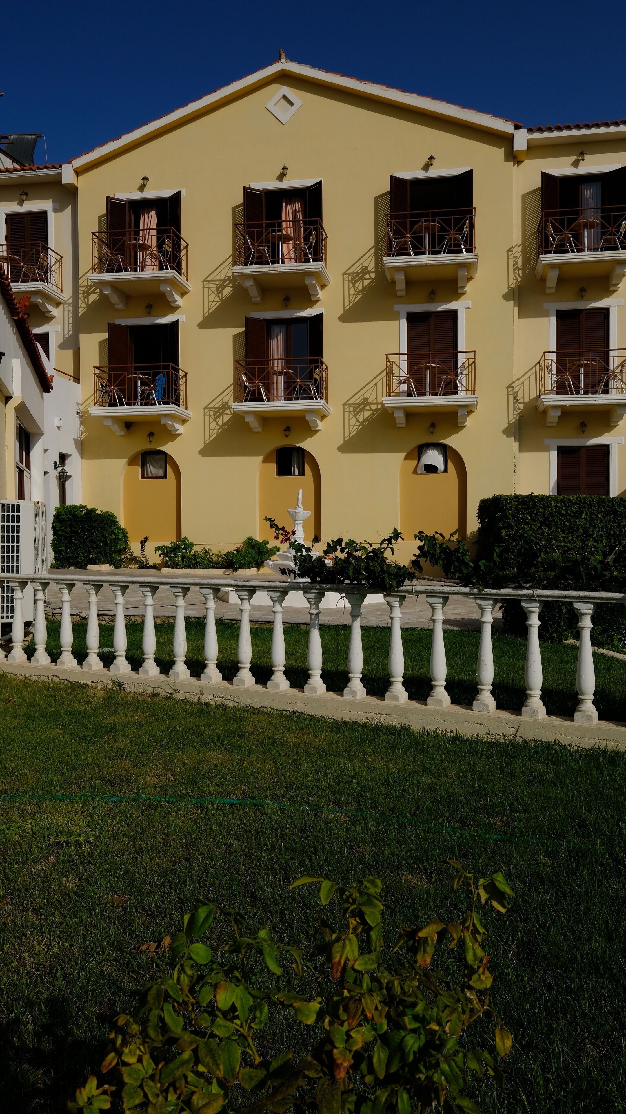 Un hotel de varios pisos con balcones, una fuente y una balaustrada blanca.