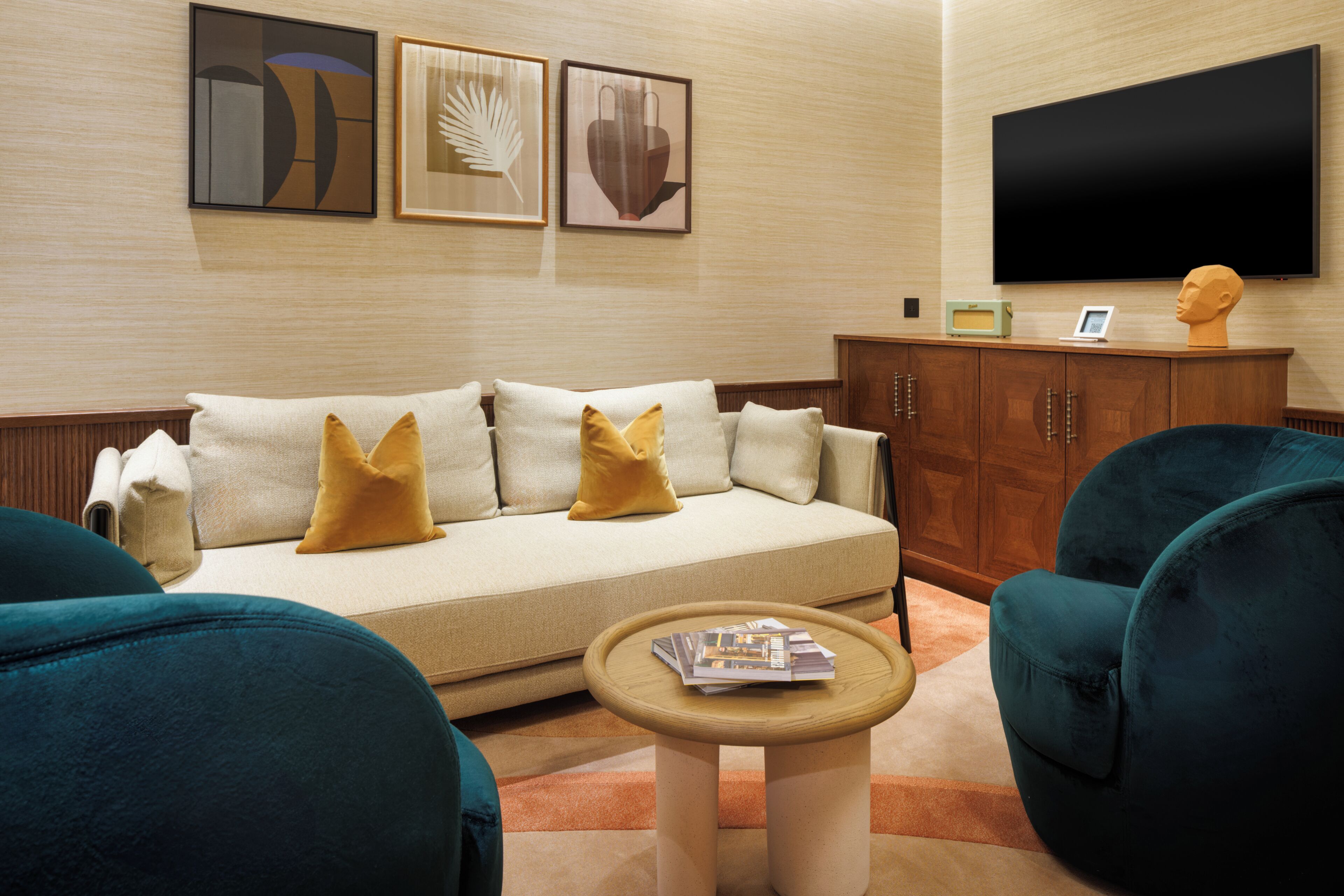 A modern living room with a sofa, two armchairs, a coffee table, and a television on the wall.