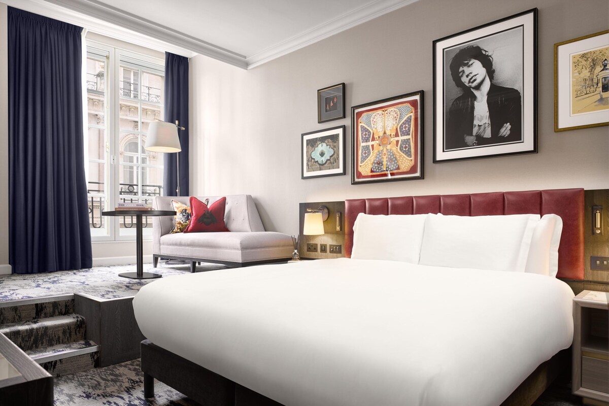 A hotel room with a large bed, a sofa, a desk, and a window with curtains.