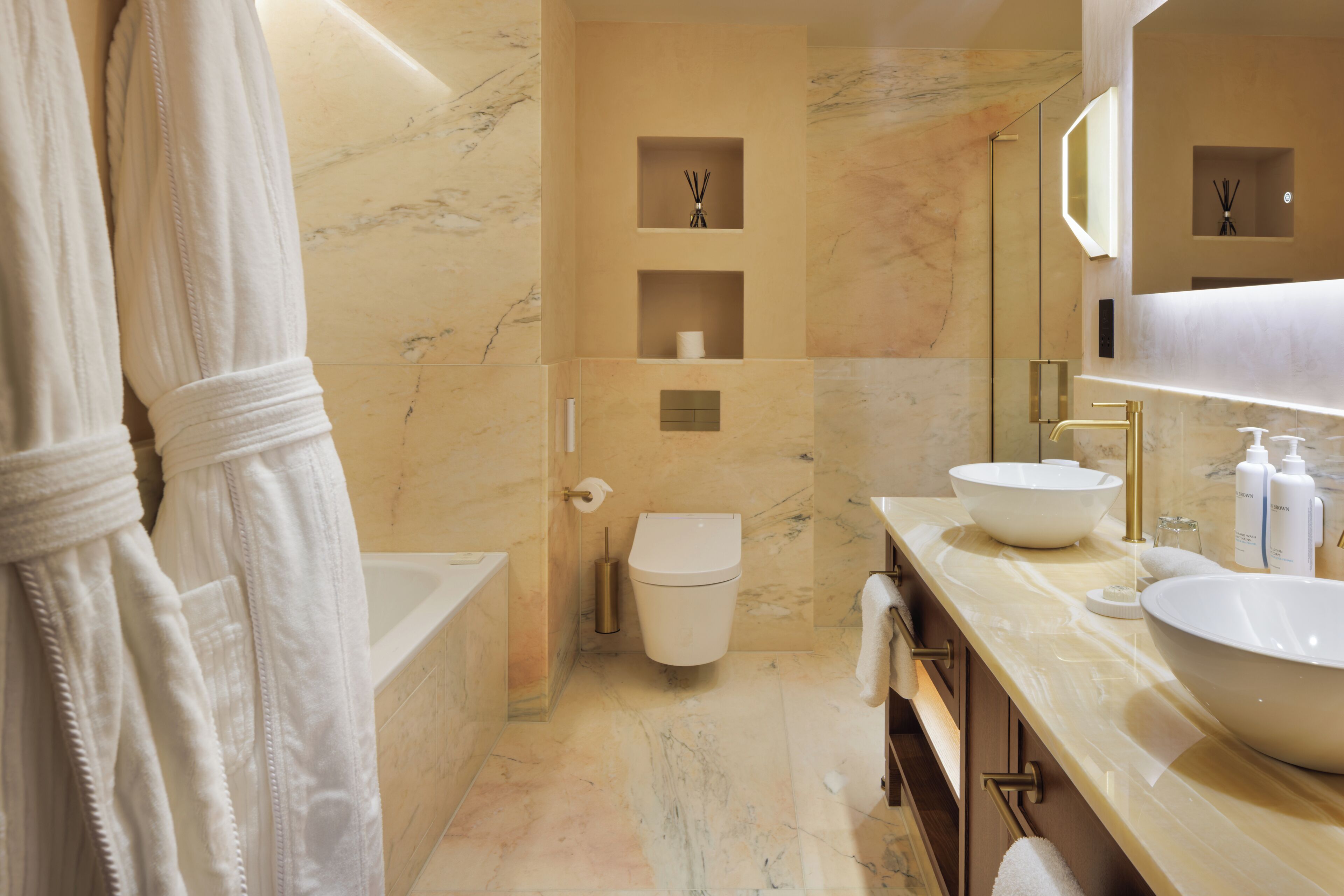 A modern bathroom with a bathtub, a large sink, and a toilet. There are shelves with toiletries and a mirror above the sink.