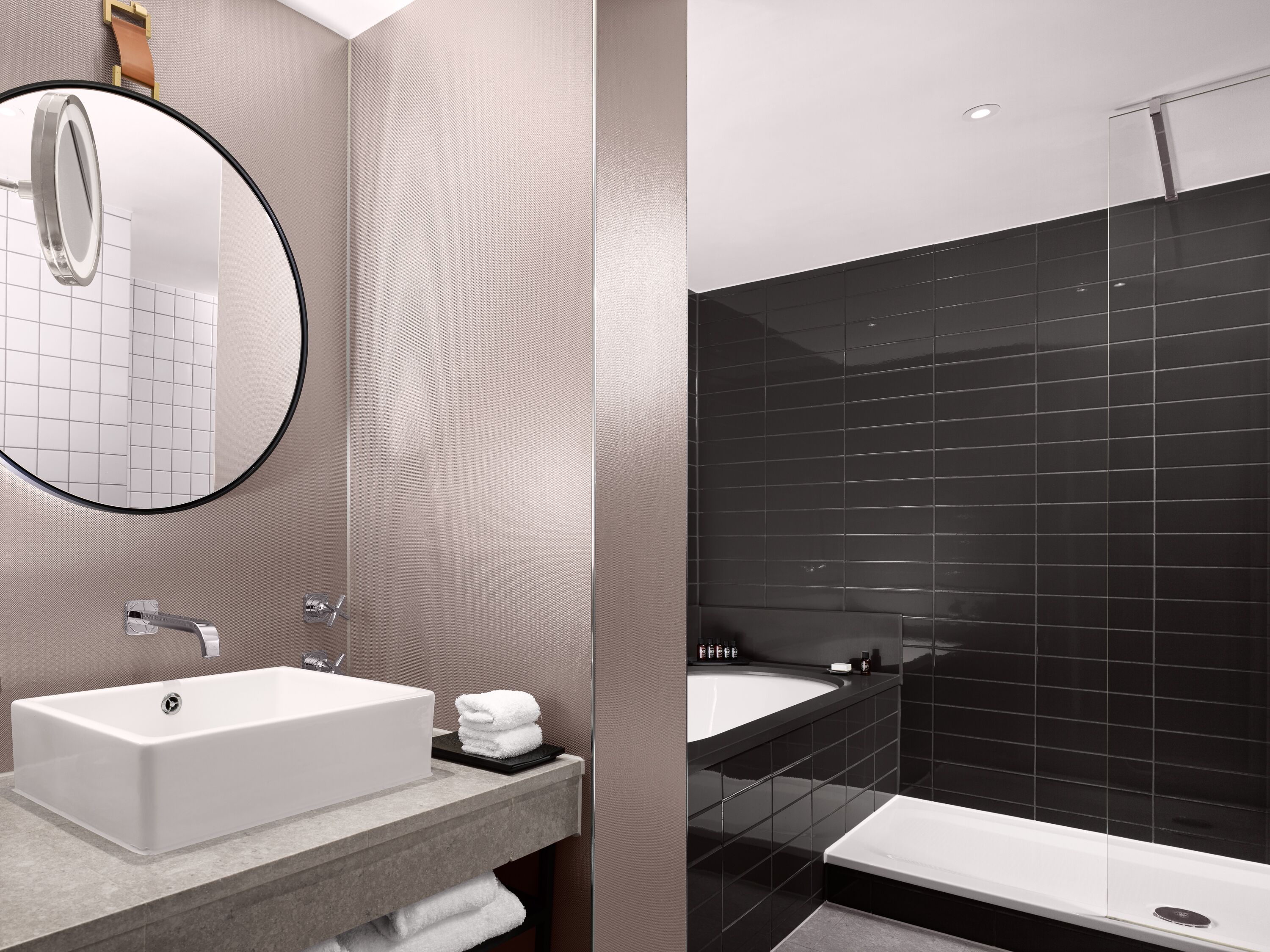 A modern bathroom with a rectangular sink, a round mirror, and a black tiled shower area.