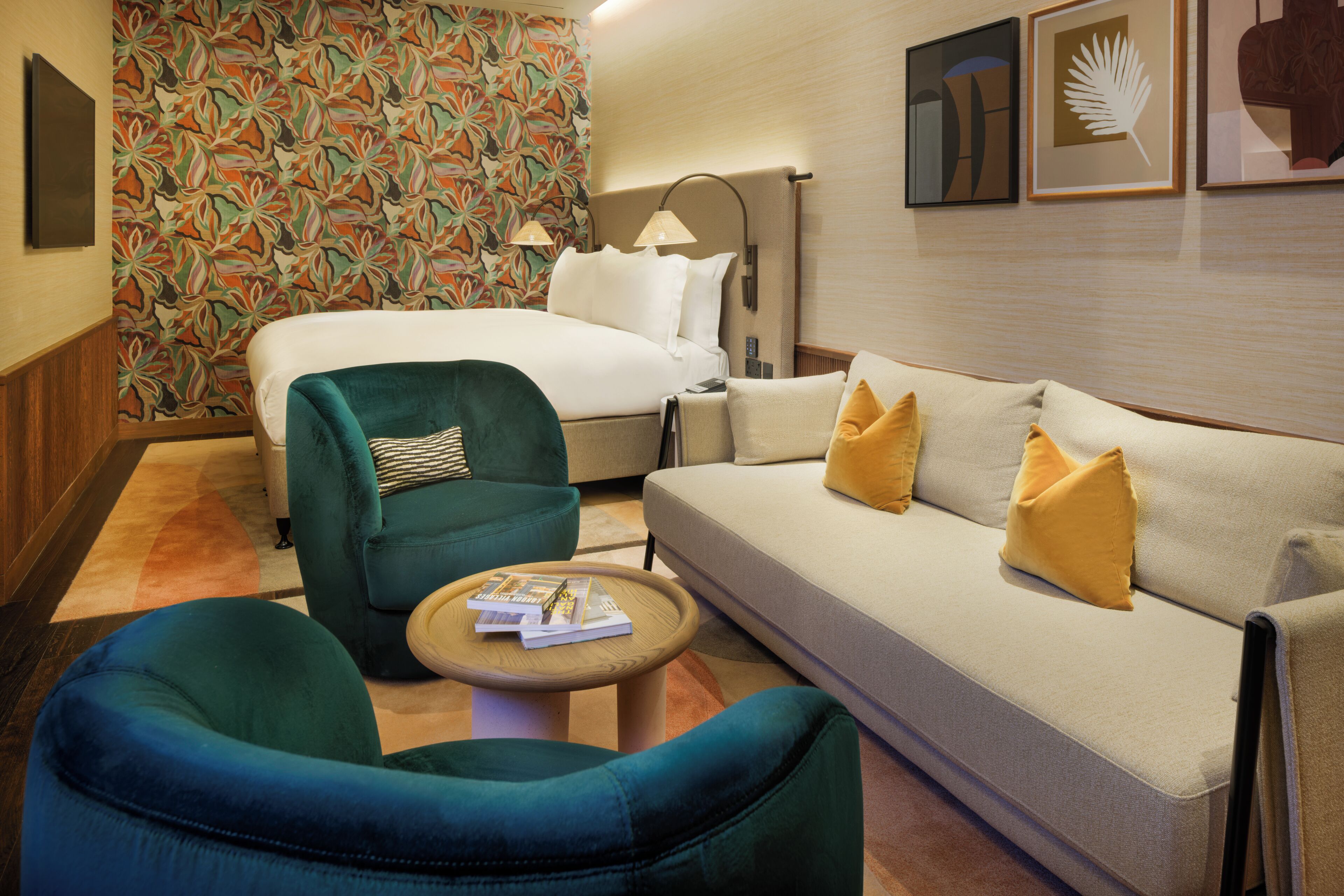 A hotel room with a bed, a sofa, two armchairs, a small table, and a patterned wallpaper.