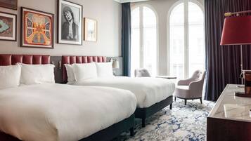 A hotel room with two beds, a desk, a chair, and large windows.