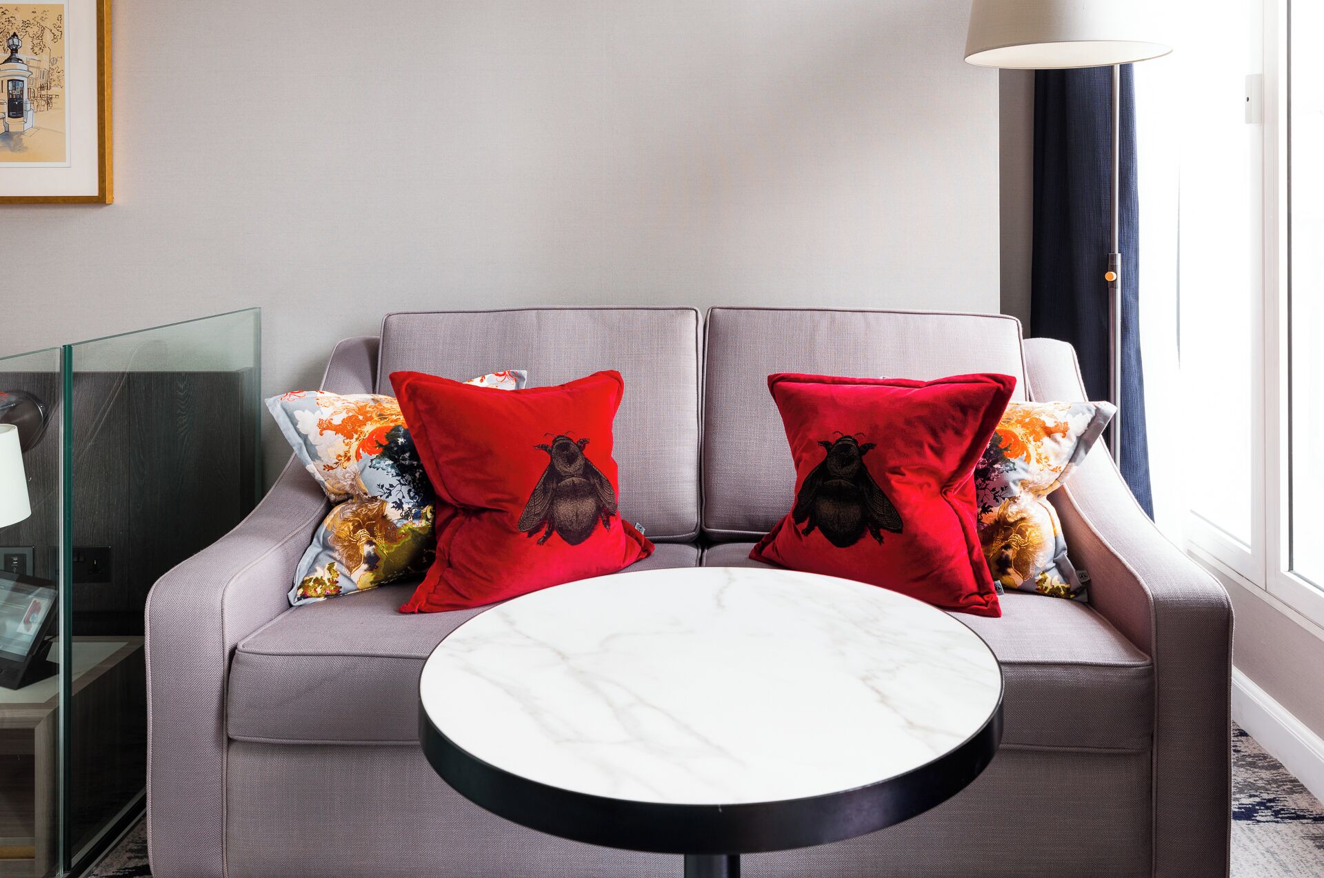 A modern living room with a grey sofa, two red pillows with owl designs, a round marble coffee table, and a glass partition.