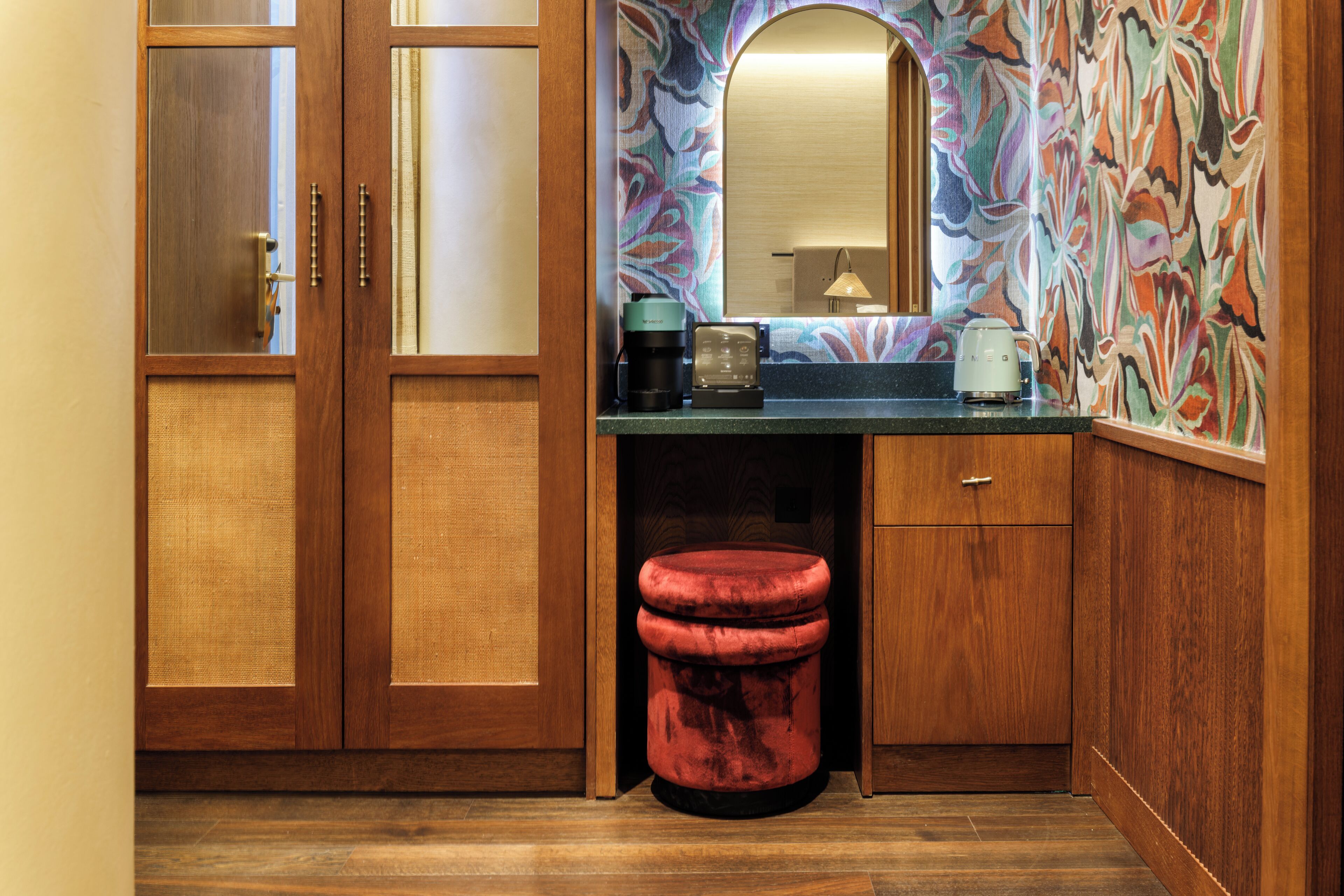 A compact bathroom with wooden cabinetry, a sink, a mirror, and a red stool.