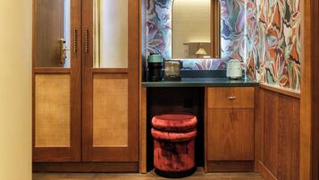 A compact bathroom with wooden cabinetry, a sink, a mirror, and a red stool.