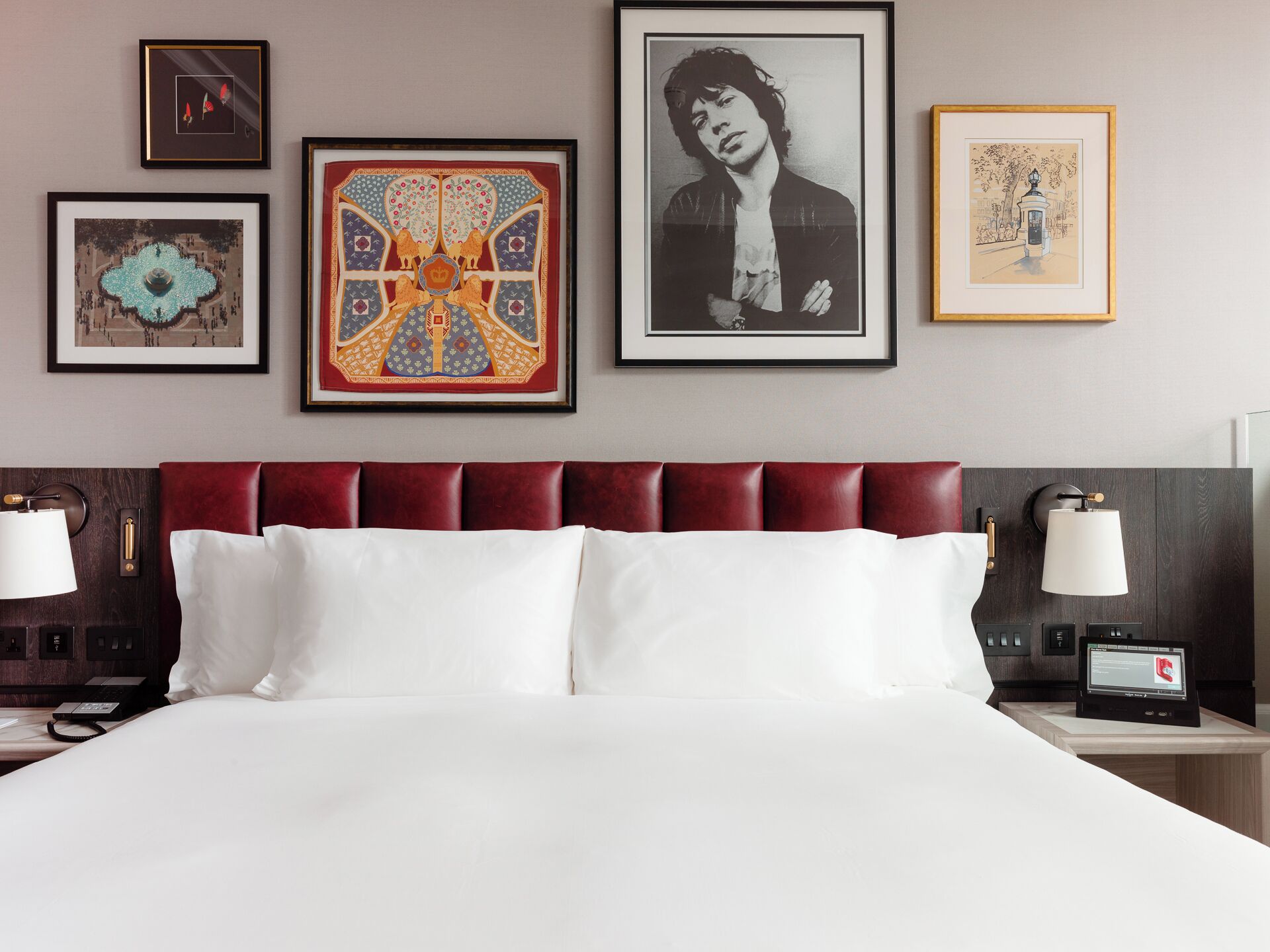 Habitación de hotel con una cama grande, dos mesitas de noche con lámparas, un televisor montado en la pared y varias obras de arte enmarcadas.
