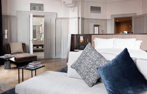 A hotel room with a large bed, a sitting area with a chair and a small table, a bathroom with a mirror and a sink, and a hallway with doors. - The Trafalgar St. James London, Curio Collection by Hilton (London)