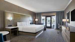 Une chambre d’hôtel avec un grand lit, des tables de chevet, un bureau, une chaise, une télévision et un balcon avec des rideaux.