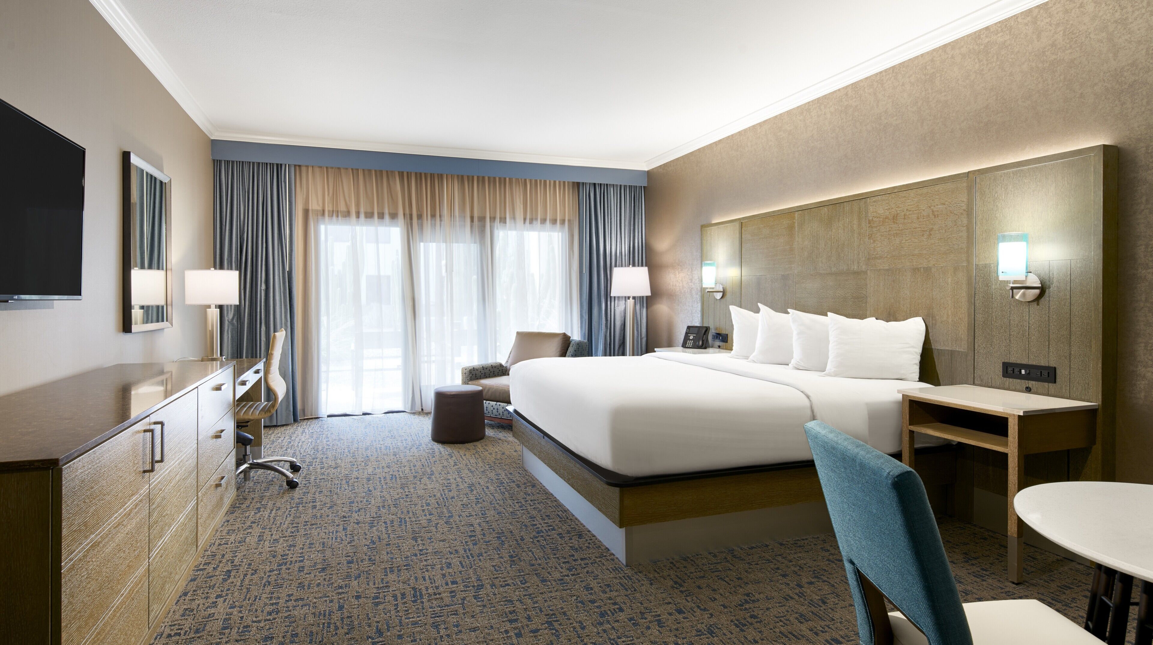 A hotel room with a bed, desk, chair, and a TV.