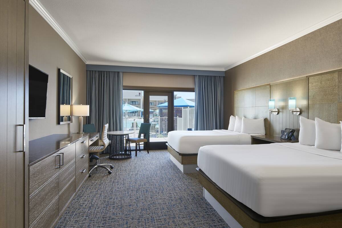 Une chambre d’hôtel avec deux lits, un bureau, une chaise, une télévision et une vue sur la ville.
