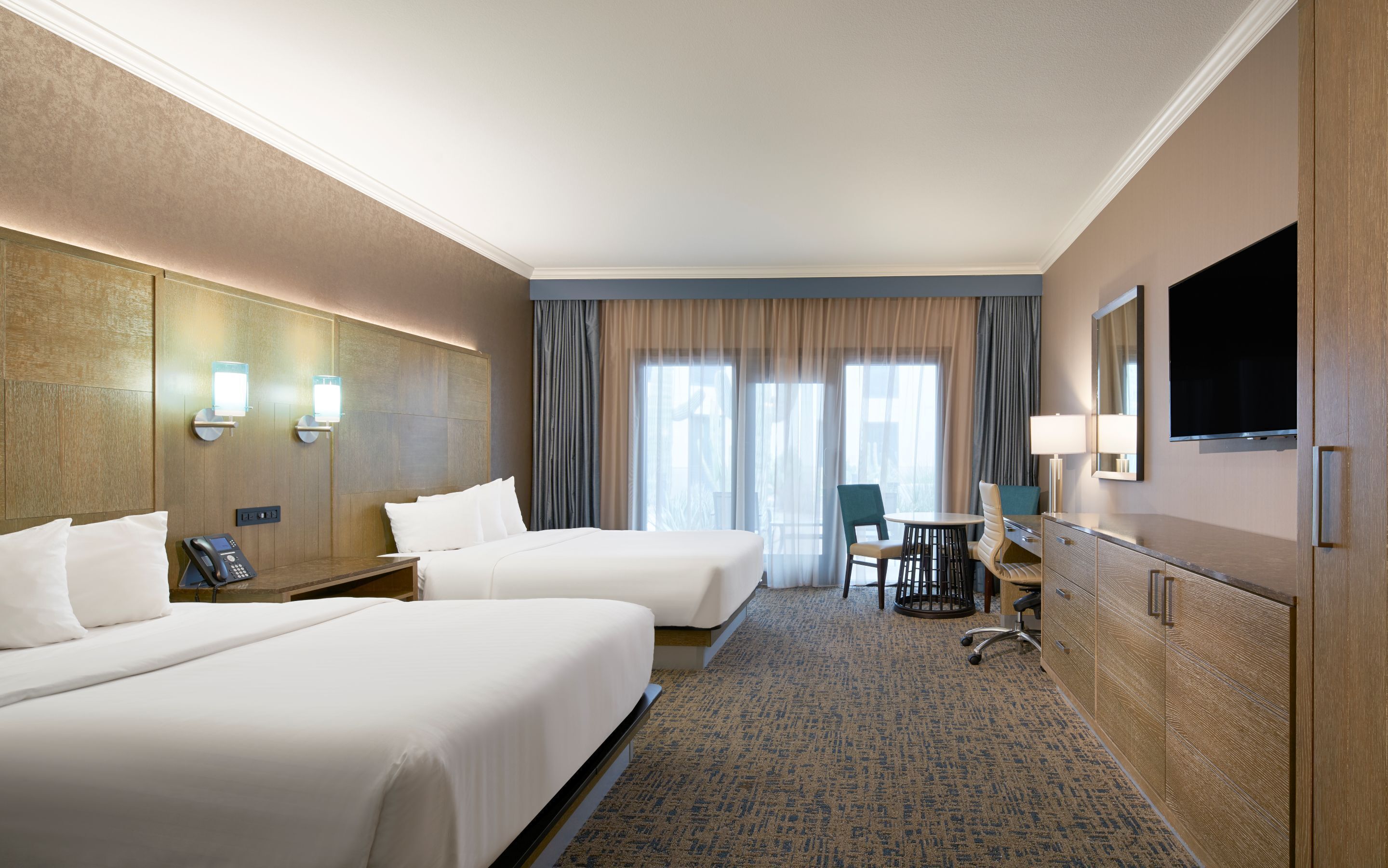 A hotel room with two beds, a desk, a chair, a TV, and a window with curtains.