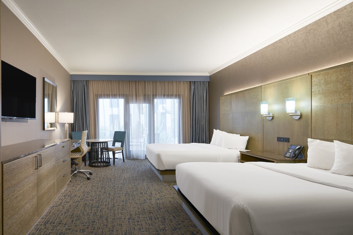 Une chambre d’hôtel avec deux lits, un bureau, une chaise, une télévision et une fenêtre avec des rideaux.