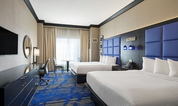 A hotel room with two beds, a desk, a chair, a TV, a phone, and a window with curtains.