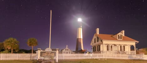 A historic lighthouse with a white picket fence, a signboard, and a house with a red roof.
