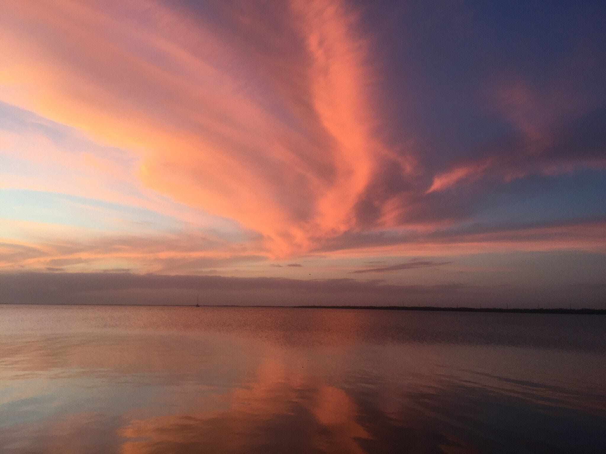A calm body of water reflecting a sunset sky with clouds.