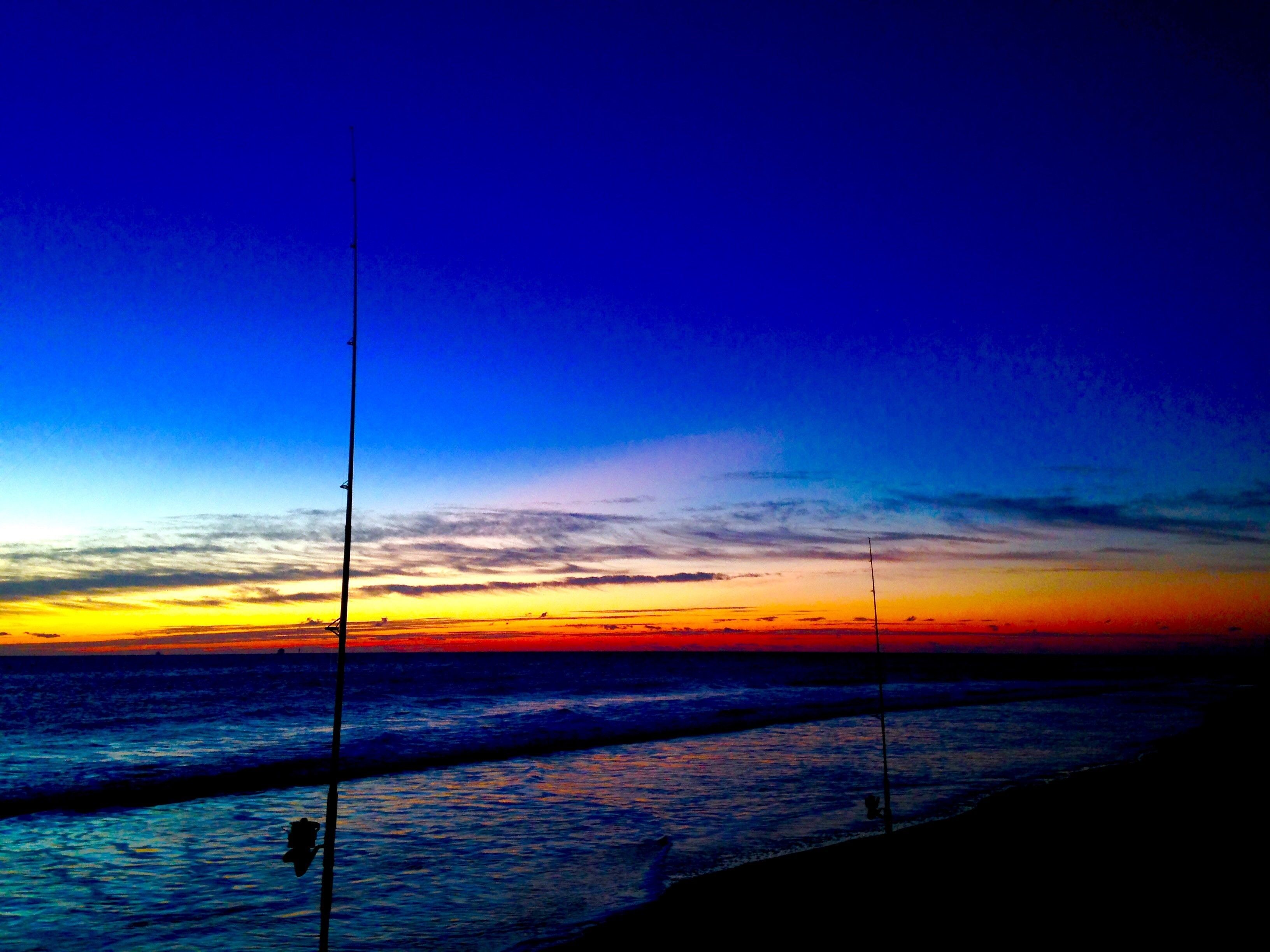 A beach scene with a sunset, calm sea, and fishing rods.