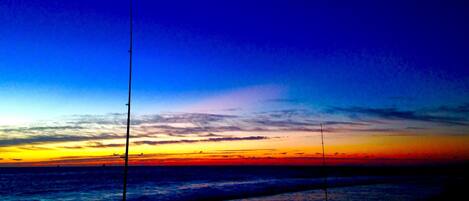 A beach scene with a sunset, calm sea, and fishing rods.