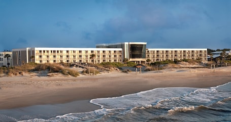 A beachfront hotel with multiple floors, a central glass facade, and a beach access walkway.