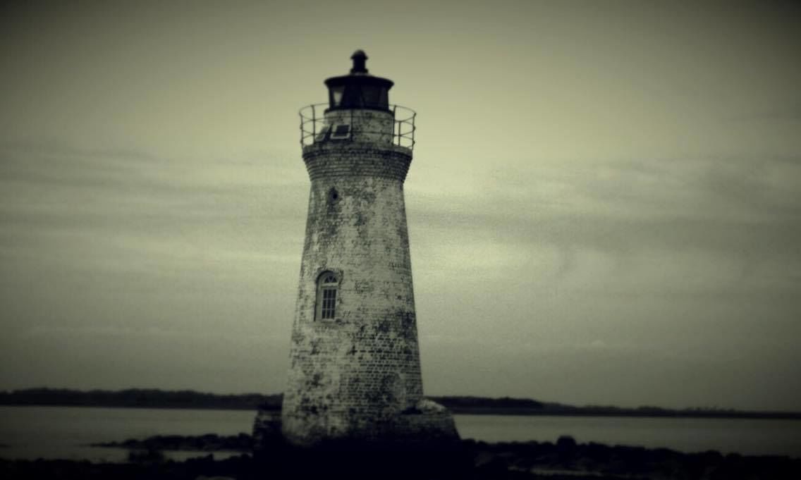 A lighthouse with a cylindrical shape, a small window near the top, and a metal railing around the upper part.