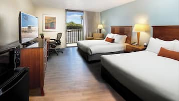 A hotel room with two beds, a desk with a computer, a TV, and a view of the beach.