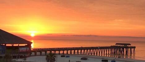 A beach with a pier extending into the ocean during sunset.