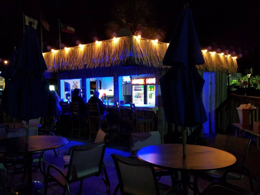 An outdoor seating area with tables and chairs, a tiki bar with a thatched roof, and a view of the ocean.