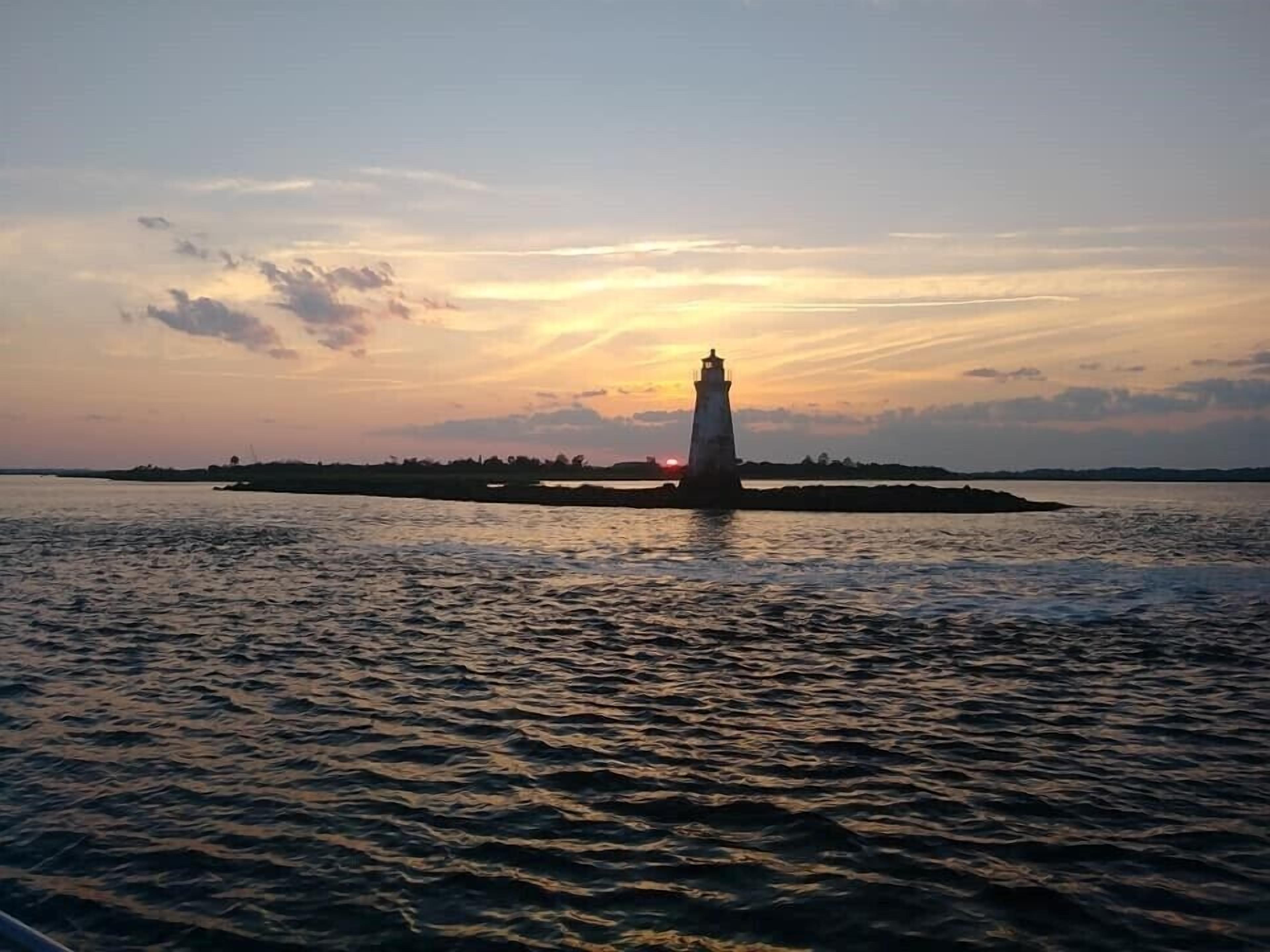 Un phare sur une petite île, avec une eau calme et un coucher de soleil en arrière-plan.