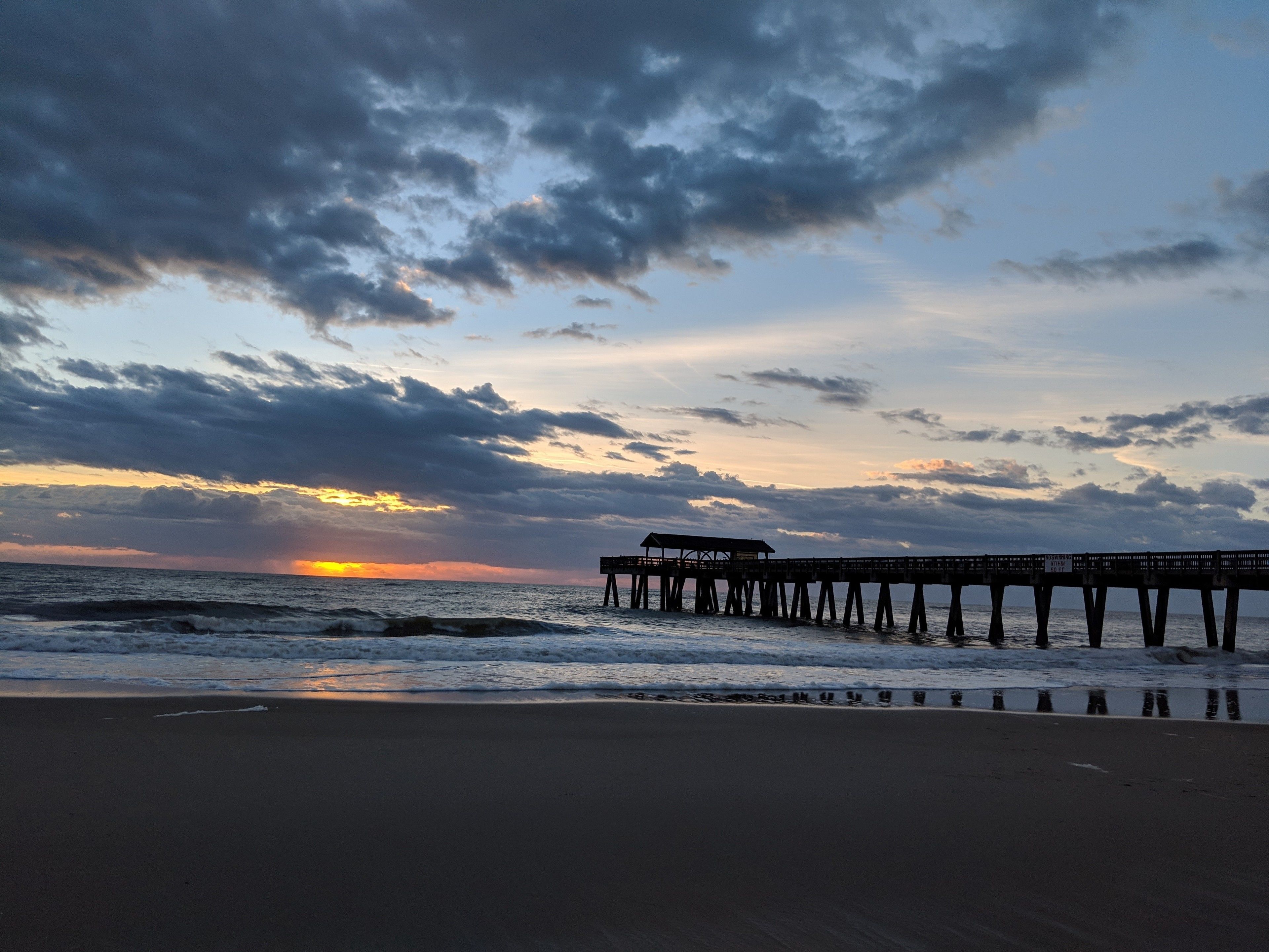 A pier extending into the ocean with a sunset in the background.