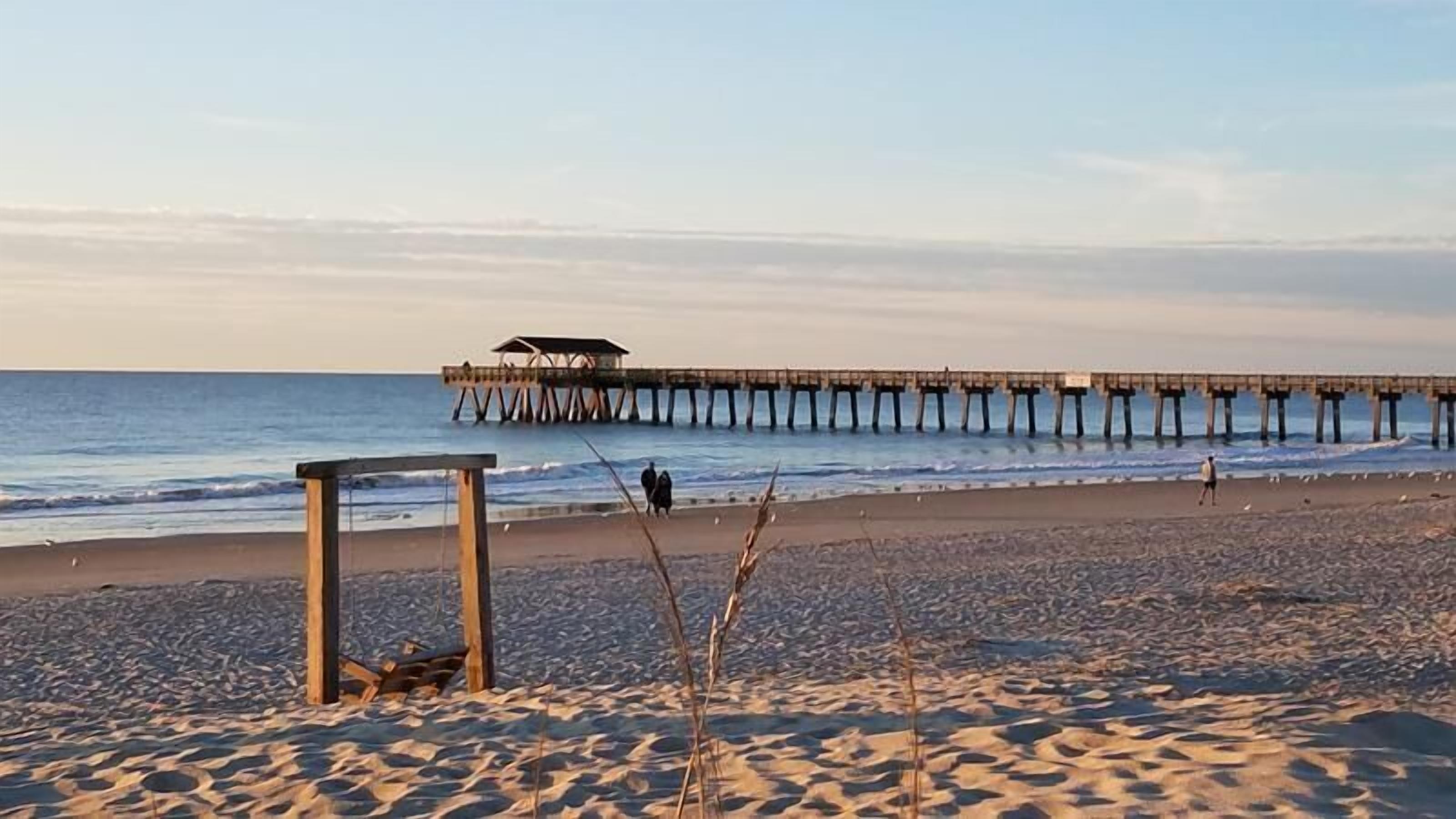 Una playa con una estructura de madera y un muelle que se adentra en el agua.