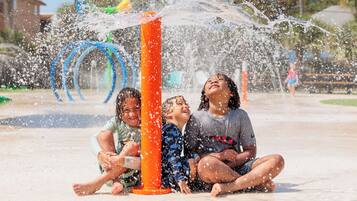 Children playing in a water fountain area with a clear sky in the background.