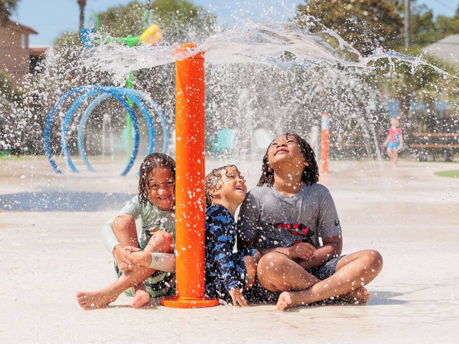 Children playing in a water fountain area with a clear sky in the background.