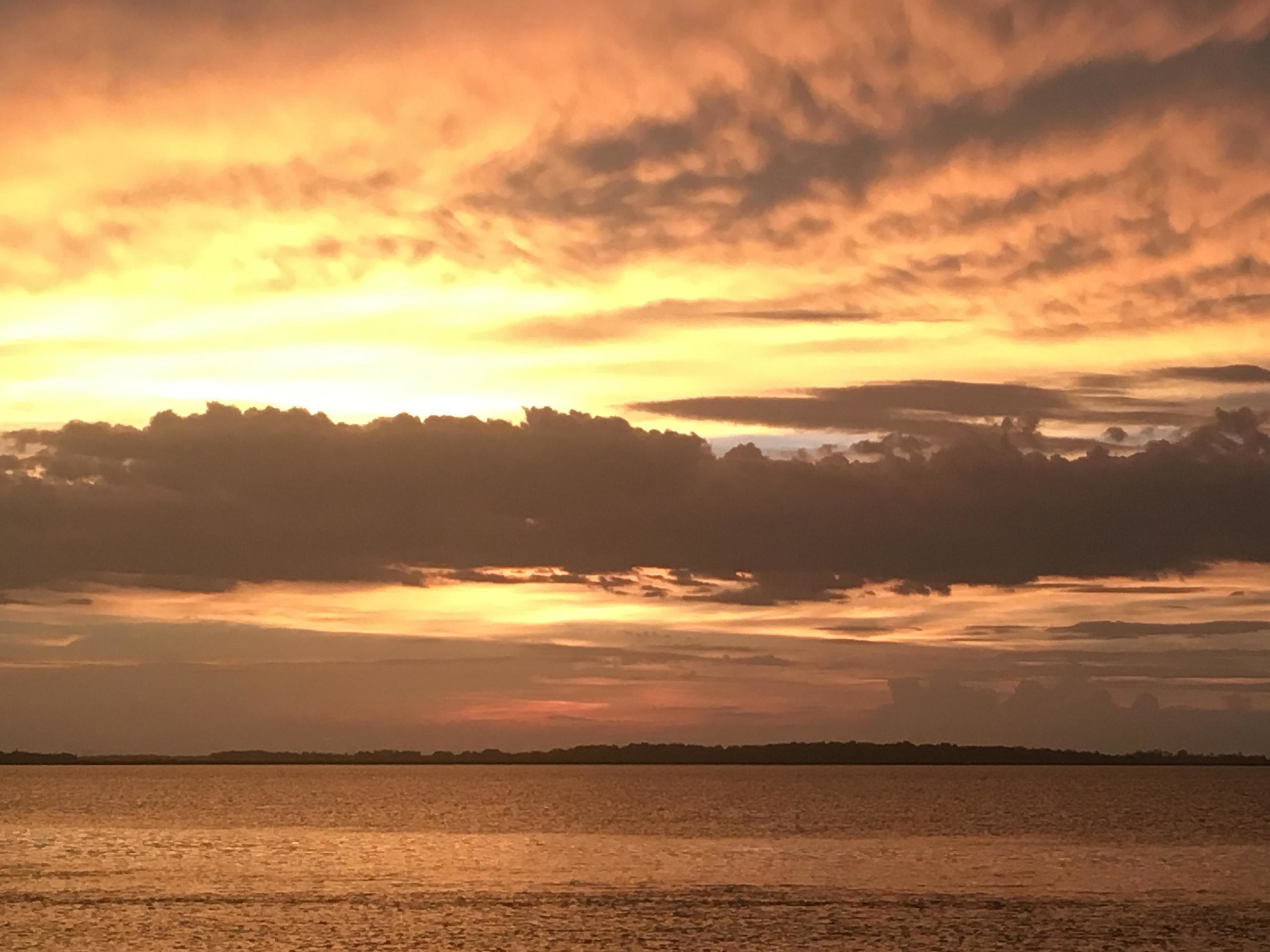 A sunset over a body of water with a distant shoreline silhouette.